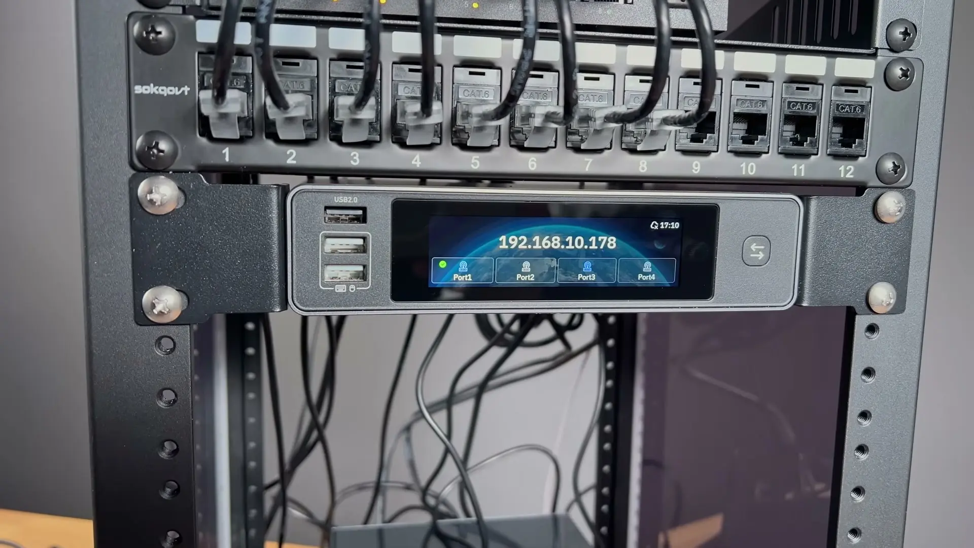 GL.iNet Comet X mounted below a 12-port keystone patch panel, with its touchscreen showing four KVM ports
